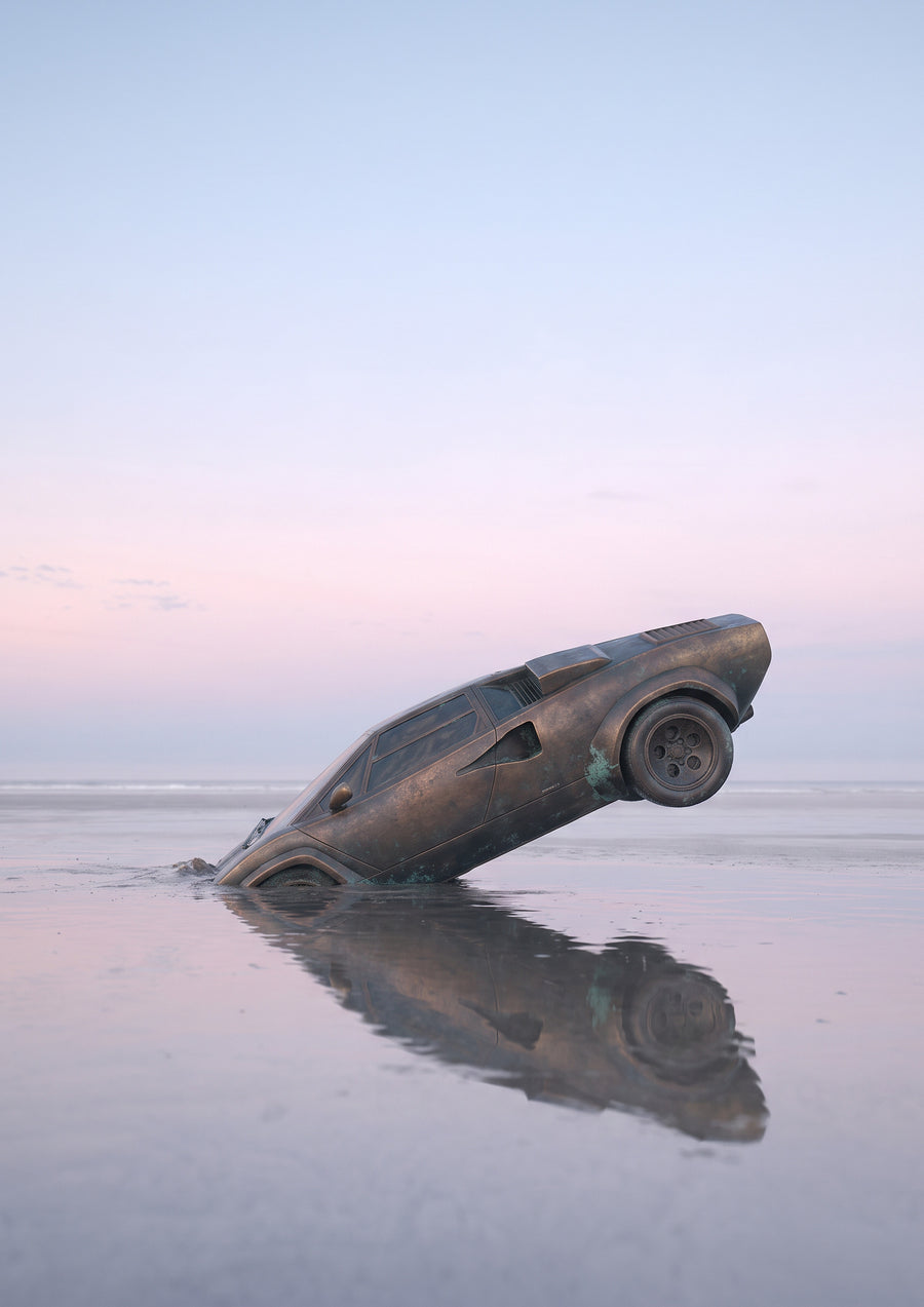 NOSTOS 01, a bronze wedge-shaped car planted nose-down in wet sand, mirrored under a pale pink sky